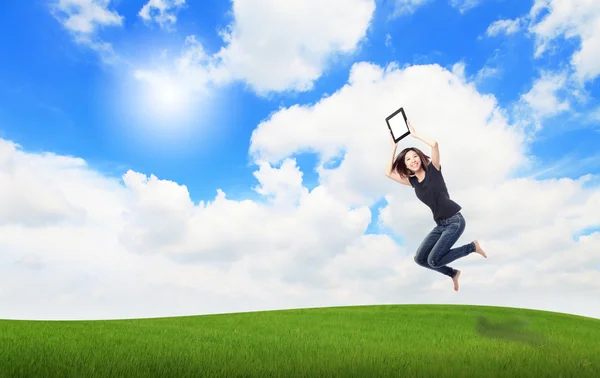 Mutlu kız atlamak ve dokunmatik yüzey bilgisayar çayır üzerinde göster — Stok fotoğraf