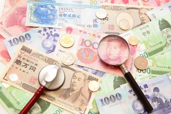Азиатская валюта, увеличительное стекло и стетоскоп на фоне — стоковое фото