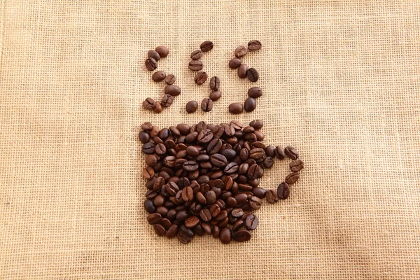 Chicco di caffè disposti a una tazza di caffè caldo su sfondo lino — Foto Stock