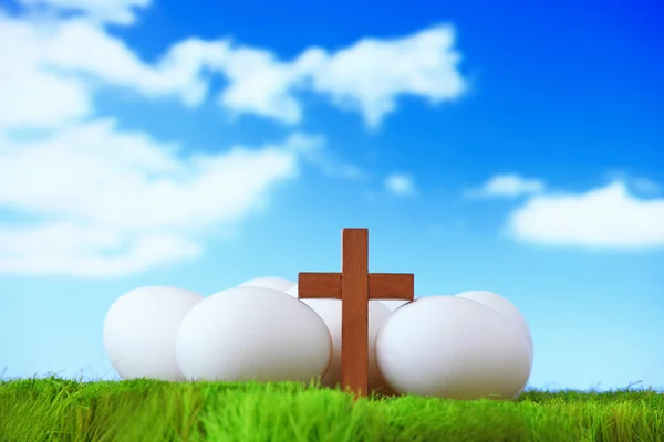 Ovos brancos e cruz de madeira na grama com céu azul — Fotografia de Stock