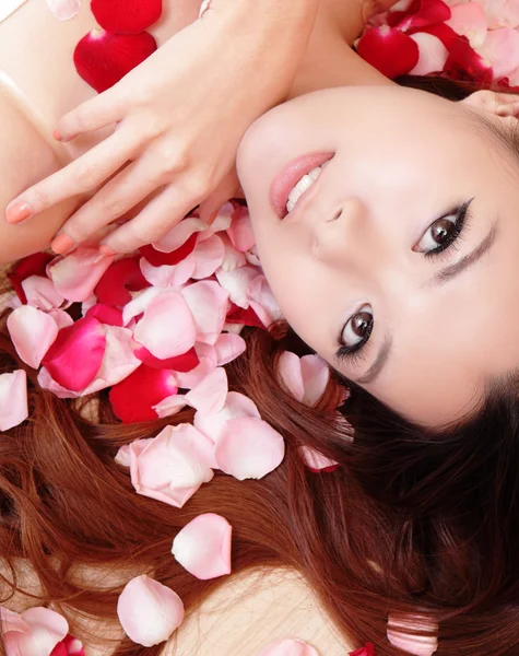 Mädchen lächelt und berührt Gesicht mit roter Rose — Stockfoto
