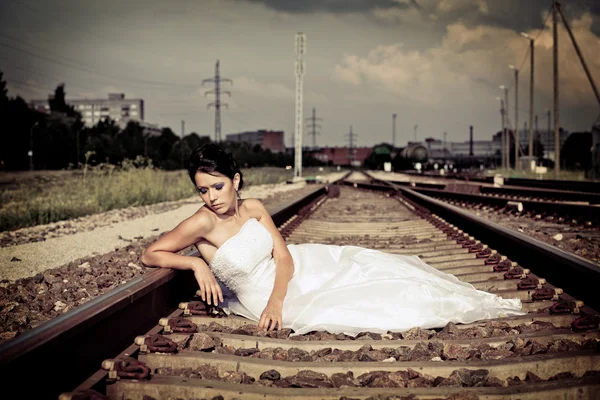 Beautiful thoughtful brunette bride is sitting on the railway and waiting — Stock Photo, Image