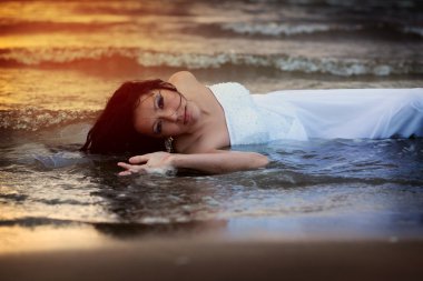 Gelinlik çekici genç kadın deniz suyu günbatımı sırasında sahiptir.