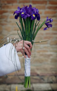 Bride is holding her wedding iris bouquet on a old castle wall background clipart