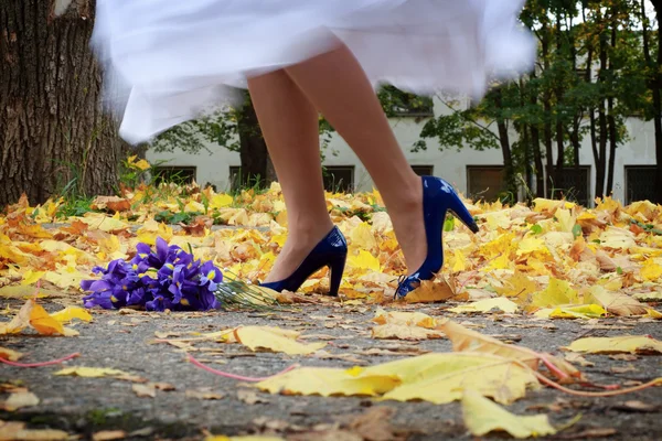 Foto d'archivio: sposa sta ballando sulle foglie gialle indossando i tacchi blu Foto Stock Royalty Free