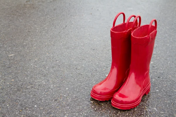 Rött regn stövlar på våta trottoaren — Stockfoto