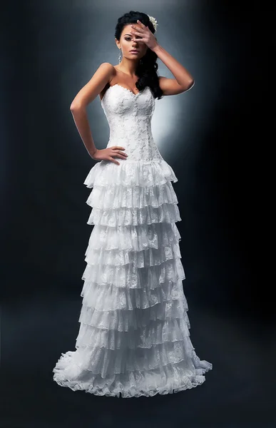 Schöne Braut Brünette in weißem Kleid steht im Studio posiert auf dem Podium — Stockfoto