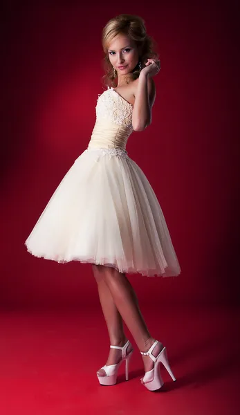 Nevěsta v bílém svatební krátké šaty na červeném pozadí stojící na pódiu — Stock fotografie