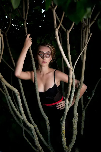 ノクターン - パーティー マスクの木の幹の間に魅力的な若い女の子 — ストック写真