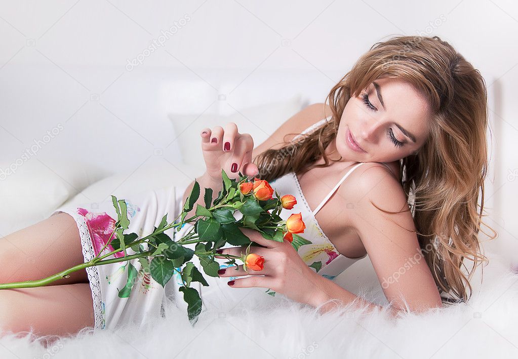 Lovely sexy girl lying in bed with branch of flower - fresh roses