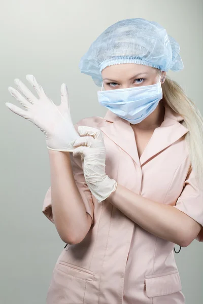 Junge Krankenschwester in medizinischen Handschuhen und Krankenhausmaske auf weißem Hintergrund. — Stockfoto