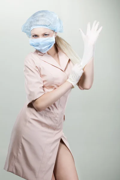 Jovem enfermeira em luvas médicas e máscara hospitalar em um fundo branco . — Fotografia de Stock