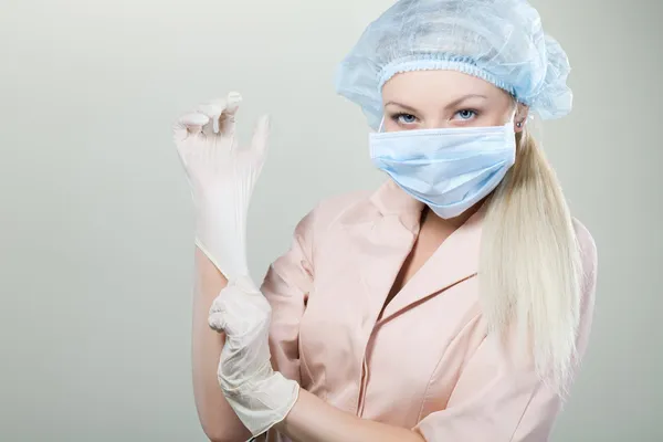 Junge Krankenschwester in medizinischen Handschuhen und Krankenhausmaske auf weißem Hintergrund. — Stockfoto