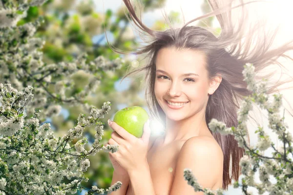 Mooi meisje in de lila bloemen met een appel in de hand — Stockfoto