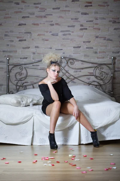 Mooie sexy meisje in zwarte jurk zittend op een bed — Stockfoto