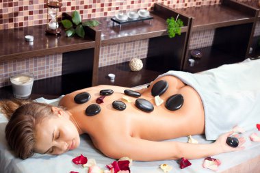 Glad woman receiving a massage with hot stone in a spa center clipart