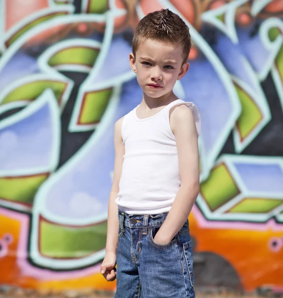 Młody chłopak z rękami w kieszeniach przeciwko graffiti ściany — Zdjęcie stockowe
