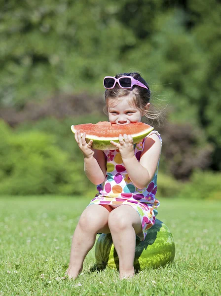 Adorable little girl sitting on a watermelon eating a slice — Stock Photo, Image
