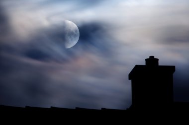 Moonlit clouds above rooftop clipart