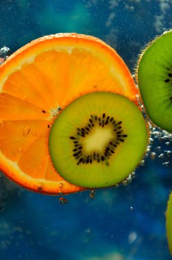 Slices of kiwi and orange in water with bubbles