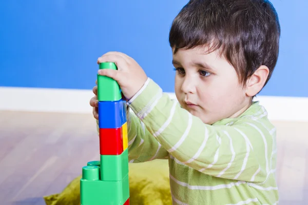 Bruneta dítě hraje s světlé bloky na dřevěné místnosti — Stock fotografie