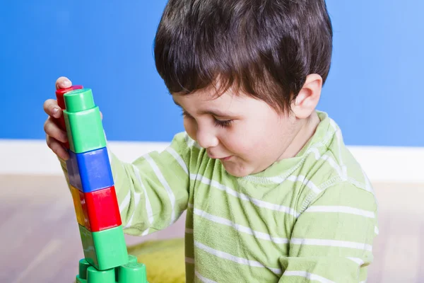 Bruneta dítě hraje s světlé bloky na dřevěné místnosti — Stock fotografie