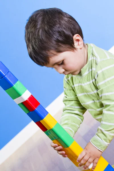 Een lachende jongetje bouwt een speelgoed blok. houten kamer — Stockfoto