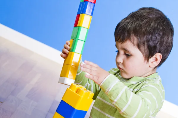 A smiling little boy is building a toy block. Wooden room — Stock Photo, Image