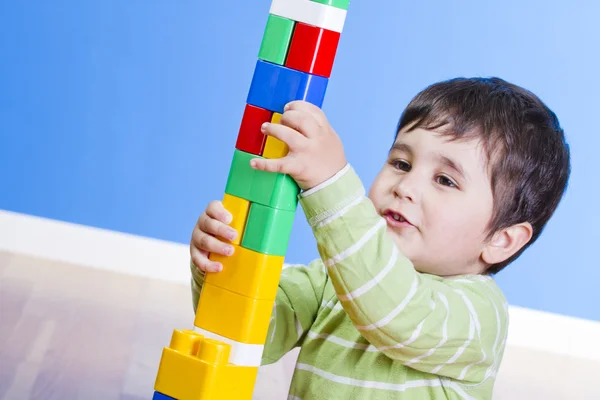 A happy little boy is building a colorful toy block tower — Stock Photo, Image