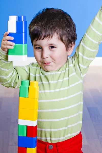 Ребенок в зеленой рубашке играет с яркими блоками, глядя вверх в сюр — стоковое фото