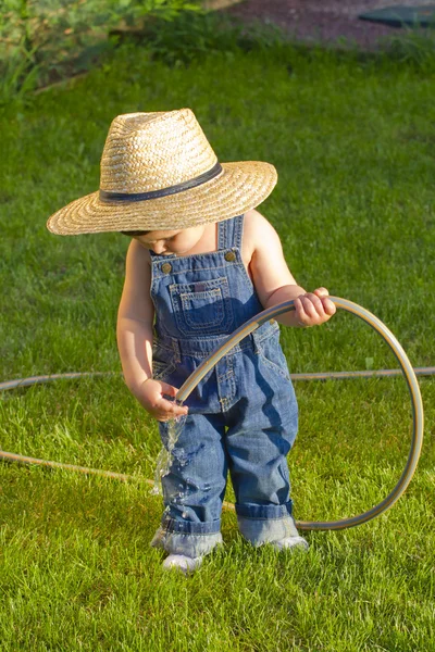 Mały chłopiec ogrodnik bawi się w jego podwórku z wężem — Zdjęcie stockowe