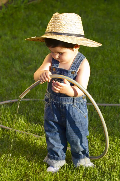 Pequeño jardinero niño jugando en su patio delantero con la manguera —  Fotos de Stock