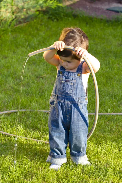 Liten pojke trädgårdsmästare leker i sin trädgård med slangen — Stockfoto