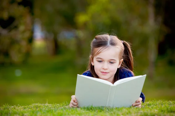 Ein kleines Mädchen genießt das Lesen im Freien auf dem Gras — Stockfoto