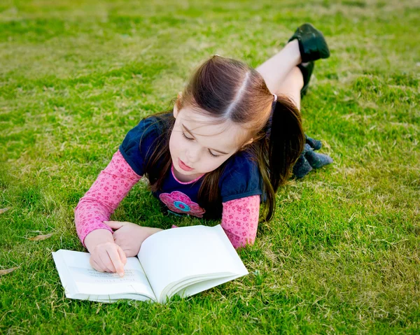 Een klein meisje lezen op het gras - uit bovenstaande — Stockfoto