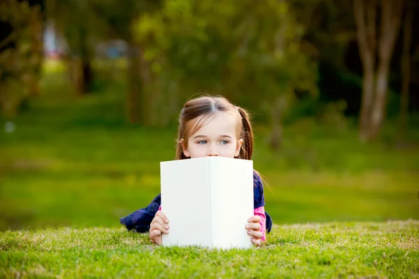 Een beetje meisje comtemplating haar lezing buiten. — Stockfoto