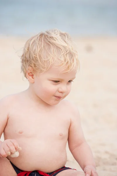 Un piccolo biondo capelli, occhi azzurri un anno vecchio ragazzo in spiaggia . — Foto Stock