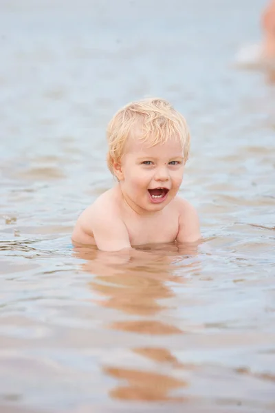 A cute little boy sits in the ocean with the ocean rippling around him — Stock Photo, Image
