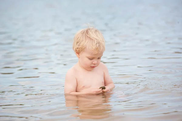 Un niño lindo se sienta en el océano con el océano ondulando a su alrededor — Foto de Stock
