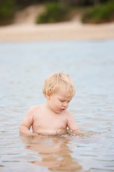 かわいい男の子の彼の周り波打つ海と海に座っています。 — ストック写真
