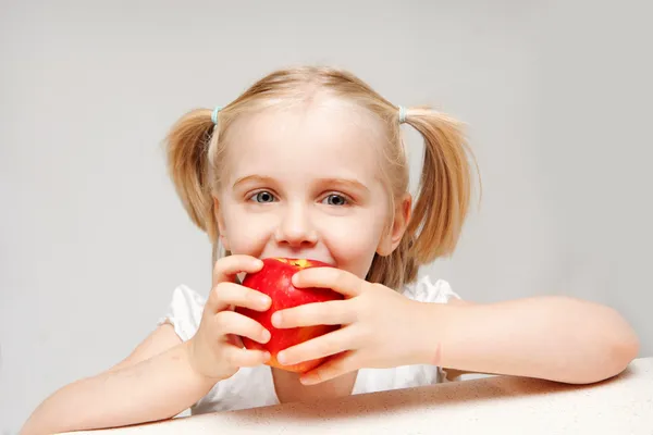 En ung flicka äter ett rött äpple — Stockfoto