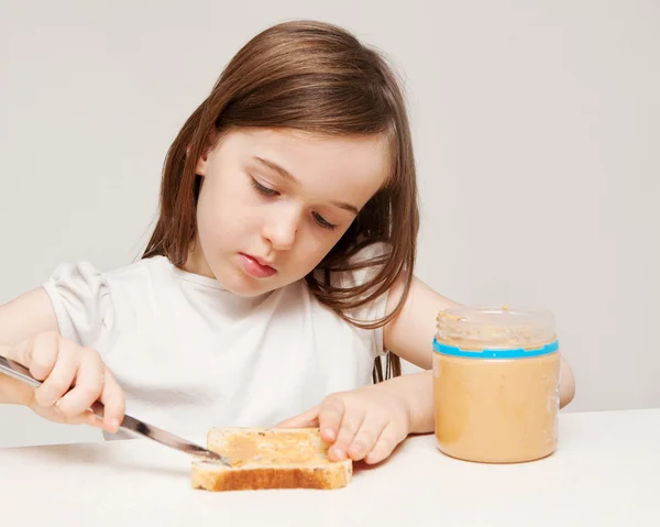 Een jong meisje maakt een boterham met pindakaas — Stockfoto