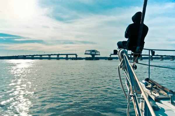 stock image Man sitting at the bow of a sailboat approaching a swing bridge