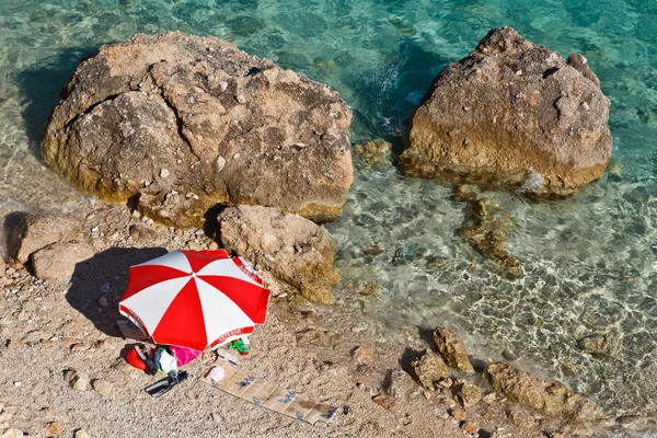 Parasol vermelho e branco na praia rochosa na Croácia — Fotografia de Stock