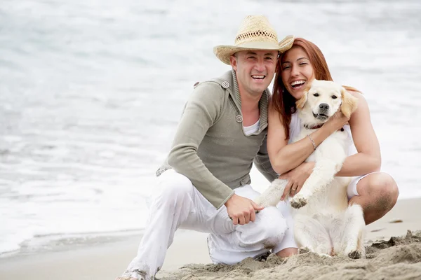Coppia giovane con un cane seduto sulla spiaggia — Foto Stock
