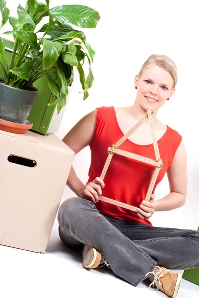 stock image Young woman with house symbol sits between move cardboards and plant