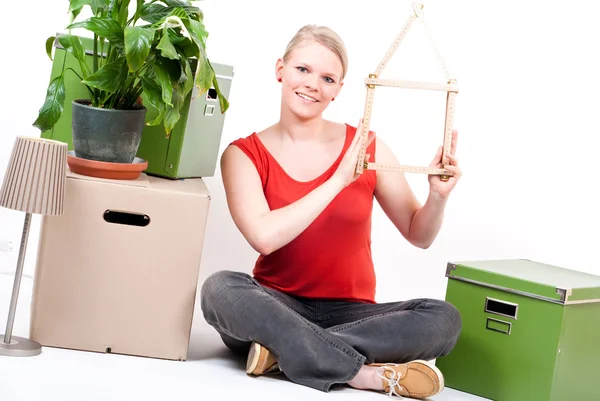 stock image Young woman with house symbol sits between move cardboards and plant