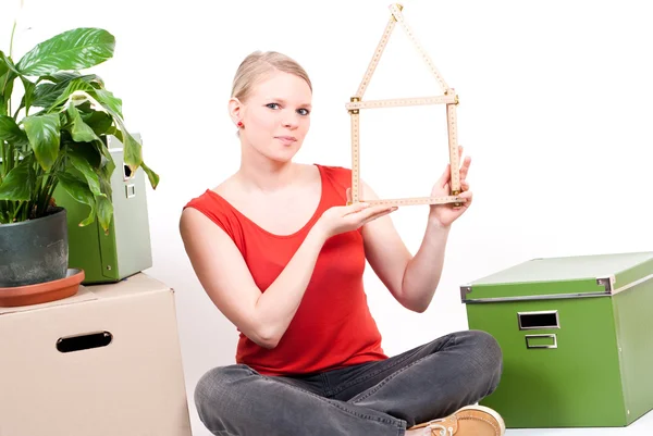 Ung kvinna med hus symbol sitter mellan flytta kartonger och plant — Stockfoto