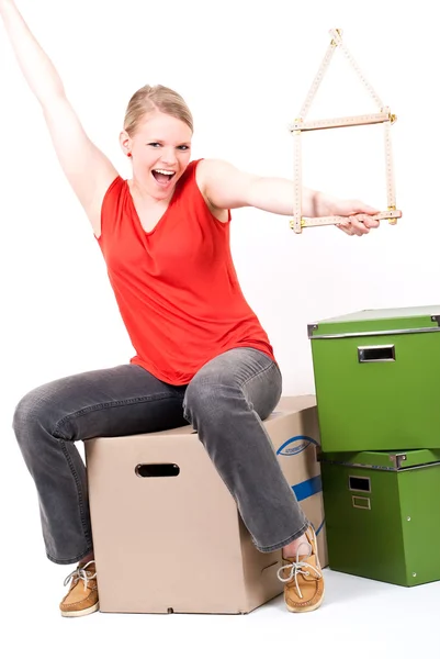 Young woman with a house symbol sits on moving box Royalty Free Stock Photos