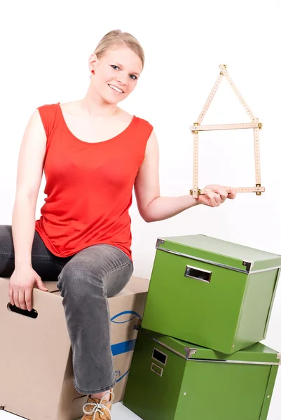 Mujer joven con un símbolo de la casa se sienta en la caja móvil Imagen de archivo